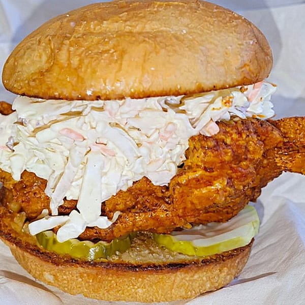 Nozzleman pizza's fried chicken sandwich with coleslaw and pickles on a toasted bun.